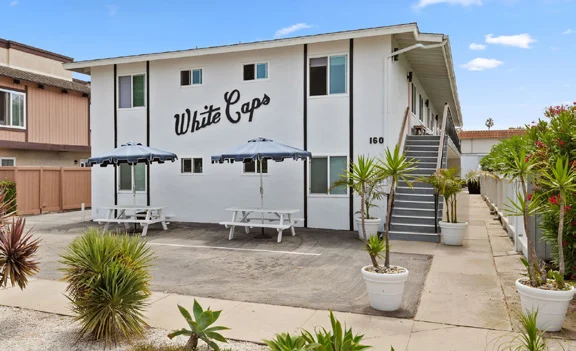 Two-story White Caps Apartments at 160 Ash Ave., Carpinteria, with patio umbrellas and picnic tables