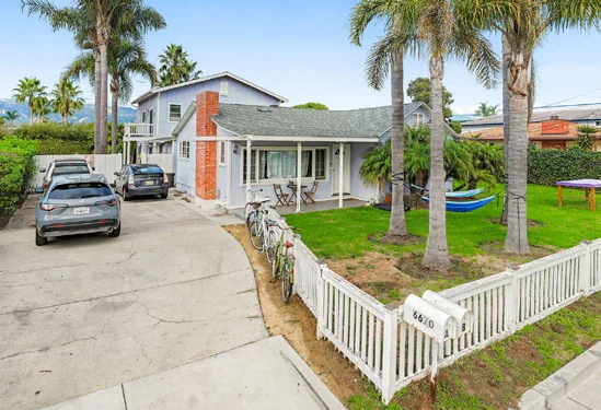 Isla Vista duplex at 6670 Sueno Rd. with a white picket fence, palm trees and parked cars